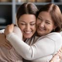 Loving middle-aged mother cuddling her grownup daughter in their living room