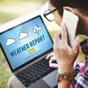 Man looking at weather report on his laptop while talking on smartphone
