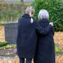 A daughter embracing her mother for comfort at a grave site in the cemetery.