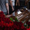 A coffin with an officer hat on it and a lot of red roses