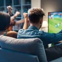 group of friends enthusiastically cheering for their team while watching a football match on TV