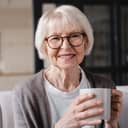 A senior woman with glasses holding a coffee mug