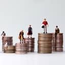 Artistic depiction of wealth inequality: Miniature people standing on piles of different heights of coins