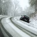 A snowed over road and a car in a ditch with skid marks behind it