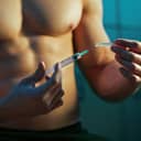 close-up of a muscular athlete in locker room with a syringe, implying the use of performance-enhancing drugs