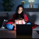 Hispanic woman eating popcorn watching a movie on the sofa depressed and worry for distress, crying angry and afraid. sad expression.