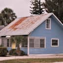 blue costal house with a corroded metal roof and jalousie windows
