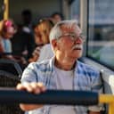 Close-up of an elderly man sitting in a bus and looking out the window.
