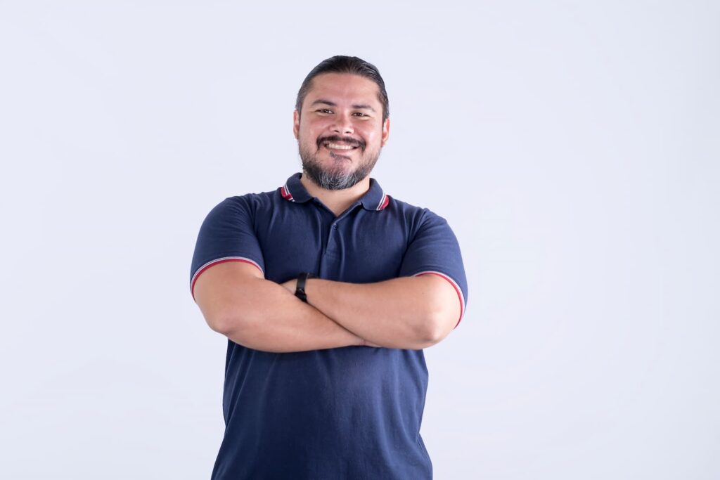 A smiling, stocky man standing with his arms folded
