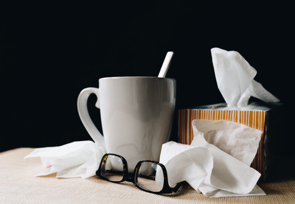 A sick person's teacup and glasses surrounded by used tissues