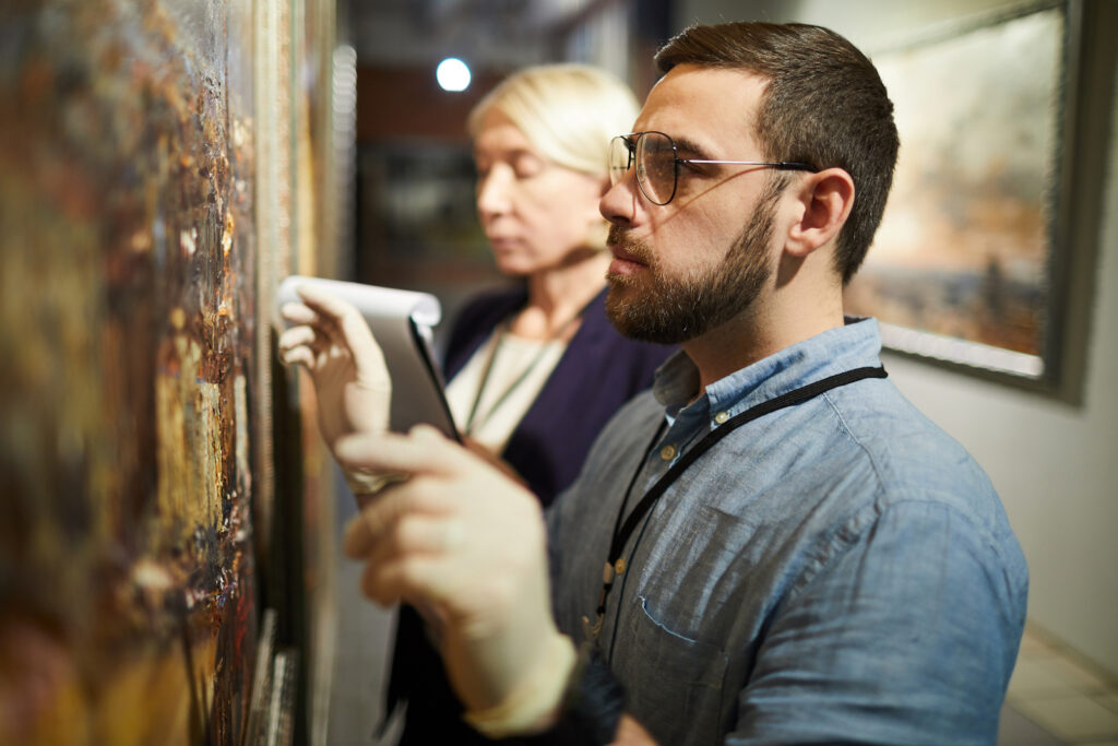 Two museum workers inspecting a painting to make sure it is authentic
