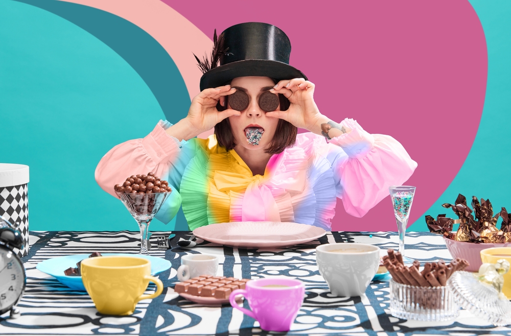 A woman in strange, colorful clothing sitting at a table covered in chocolate and sweets