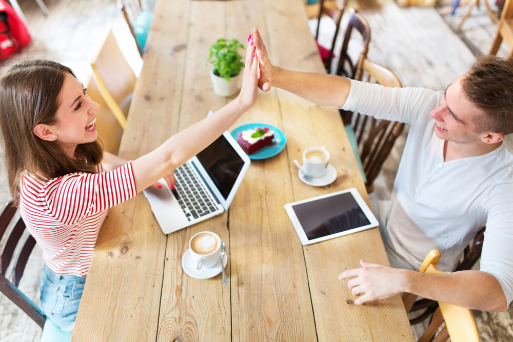 A man and woman high-fiving each other across a table while working together on a project